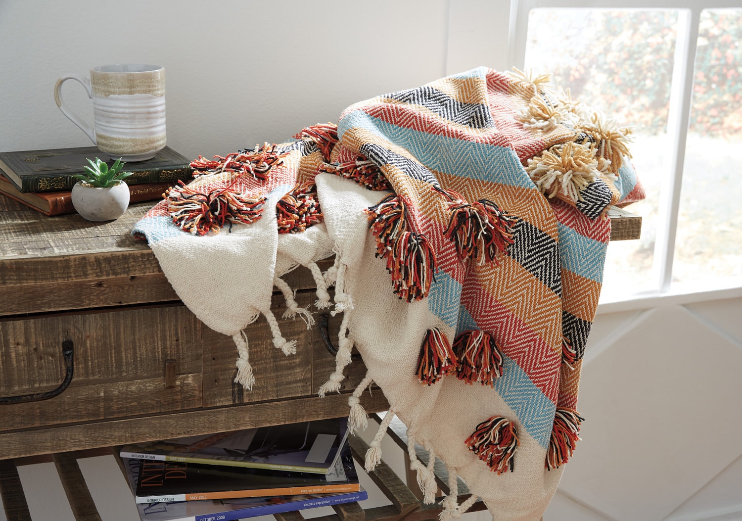 Colorful throw blanket with tassels draped over a rustic wooden table