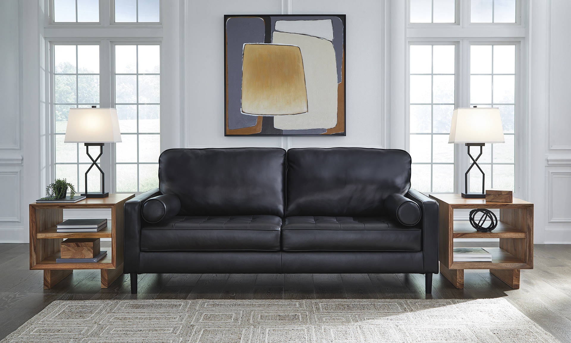 Modern living room with black sofa, wooden side tables, lamps, and a large painting above the couch