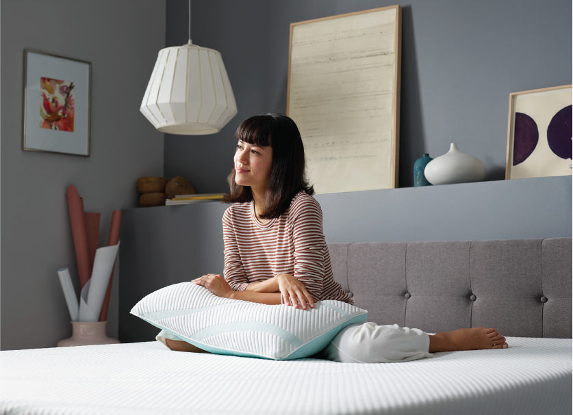 Woman sitting on a bed in a stylish bedroom, looking thoughtful