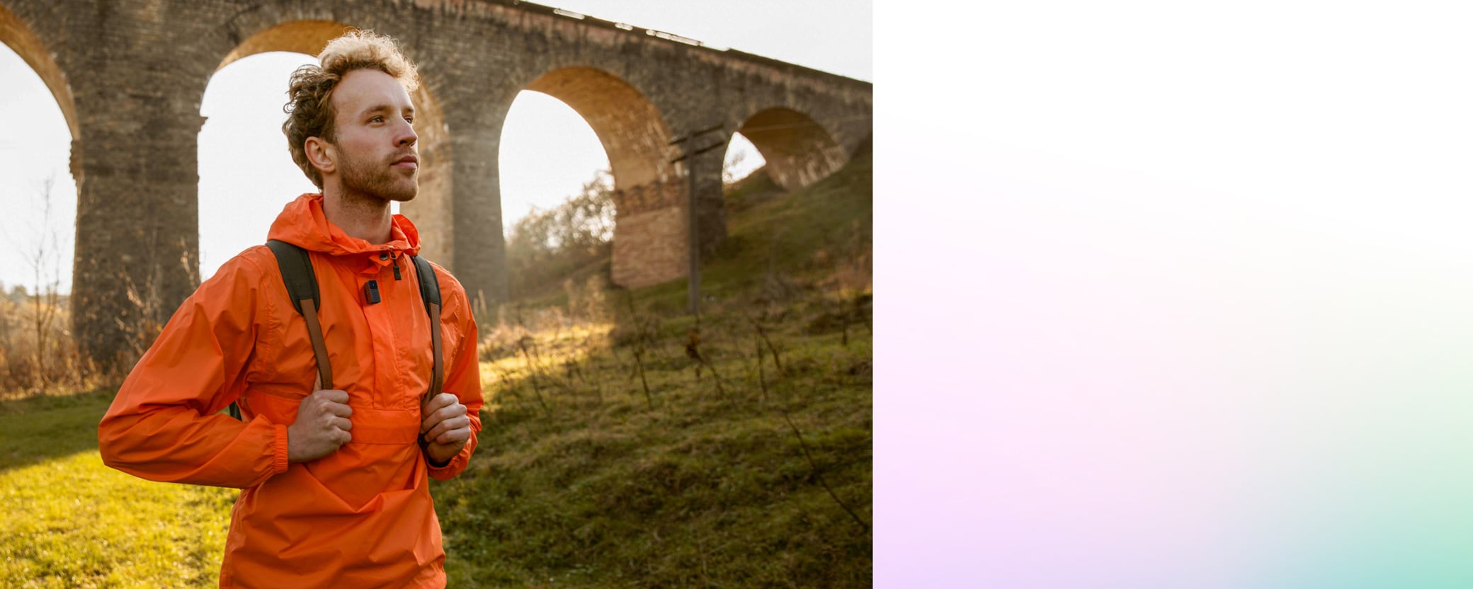 Man in orange jacket hiking near old stone aqueduct