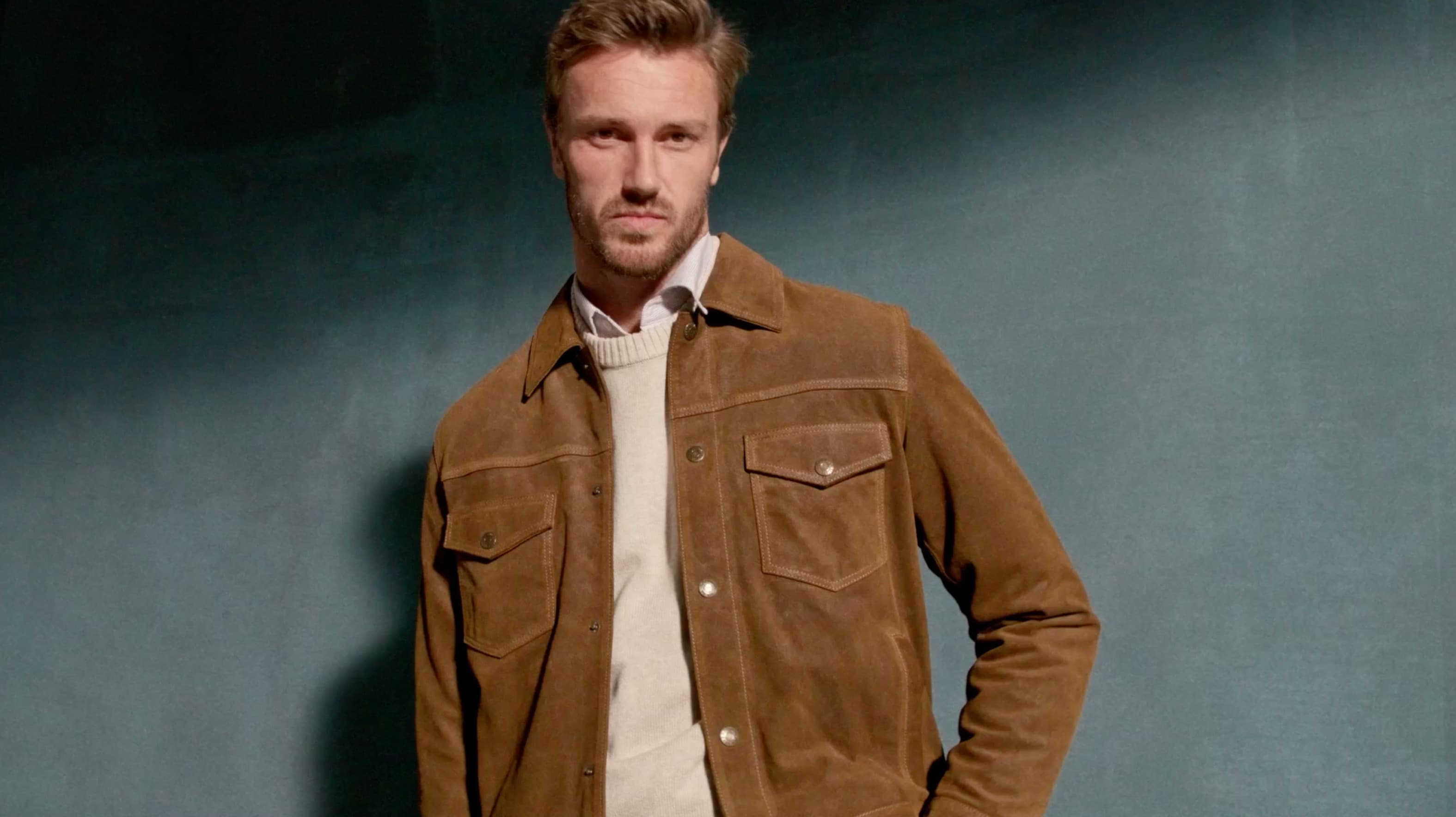 Man in a brown jacket posing confidently against a dark background