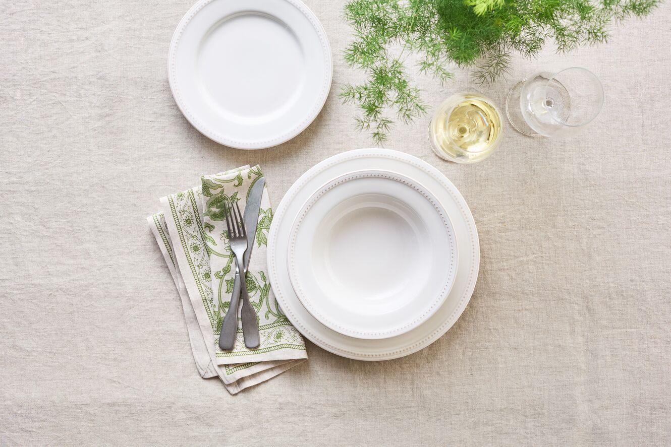Elegant table setting with white plates, cutlery, a glass, and greenery on a linen surface