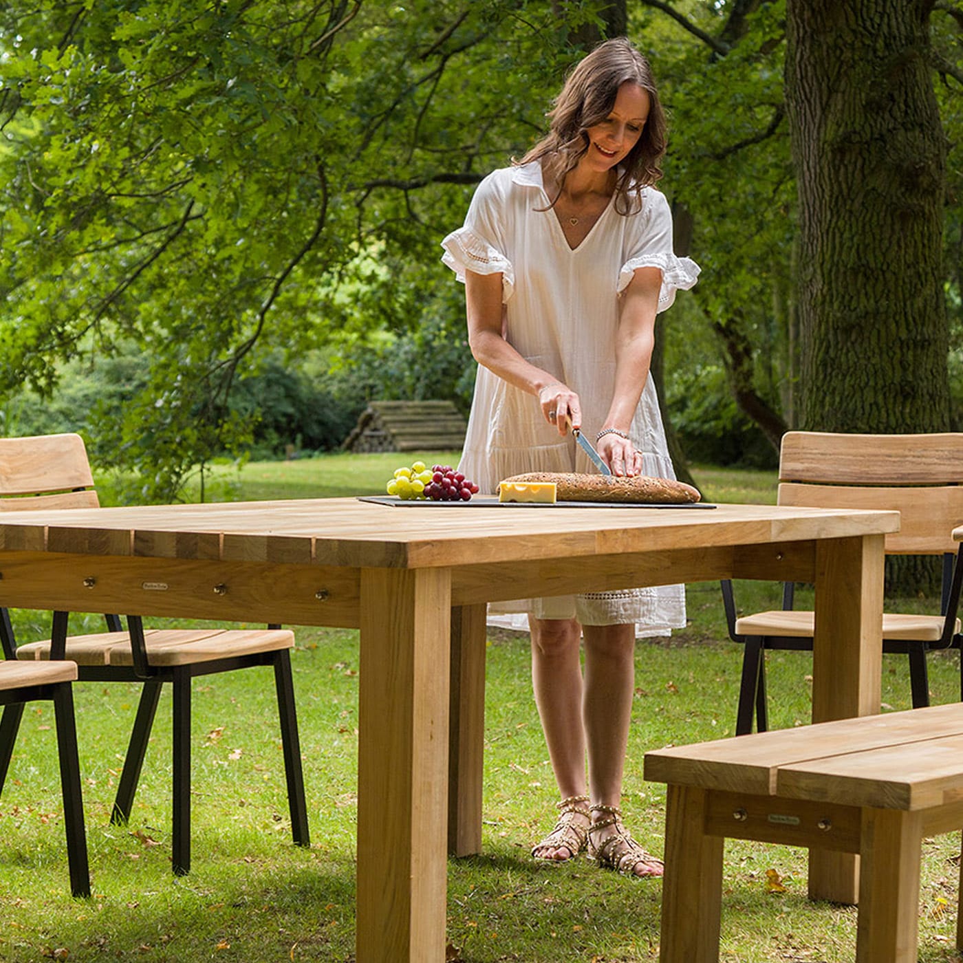 Woman in white dress setting a wooden table outdoors