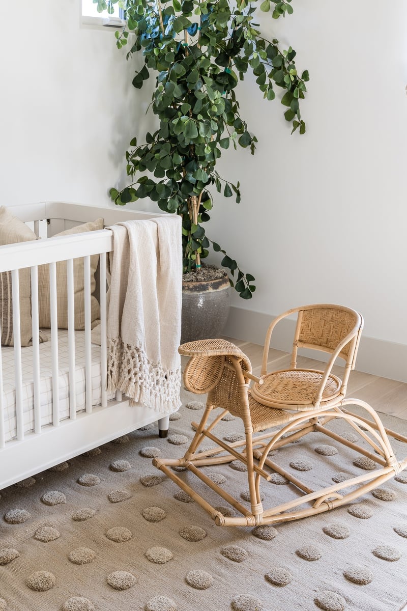 A serene nursery room with a white crib, rocking chair, and a large potted plant