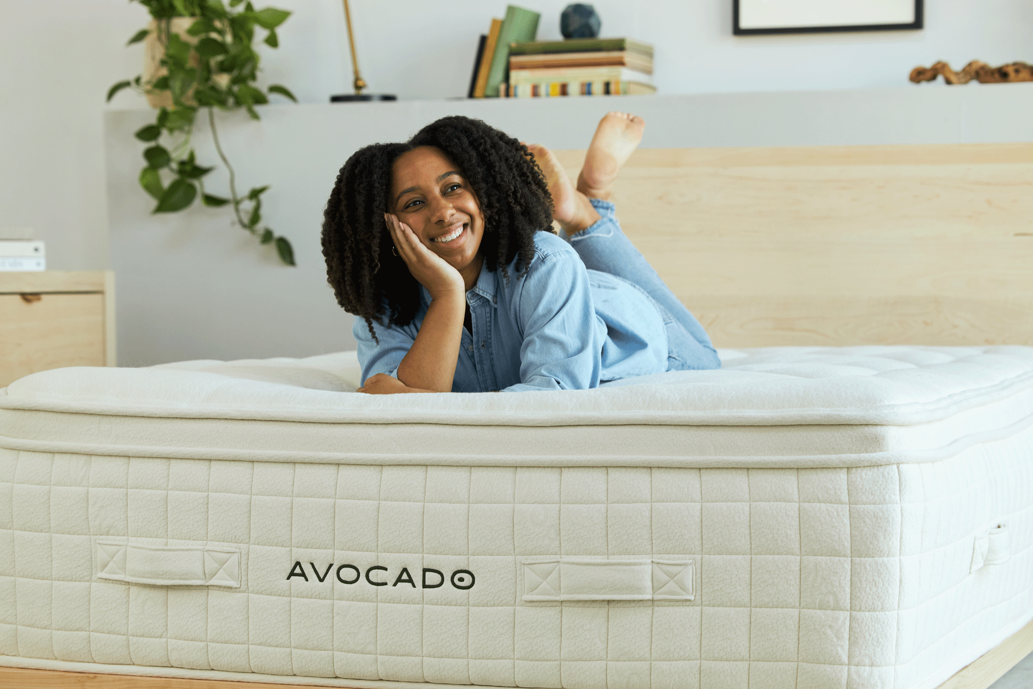 Happy woman lying on an Avocado brand mattress in a bright bedroom