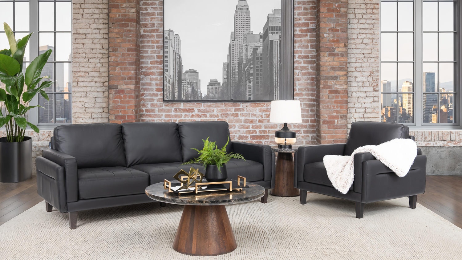 Modern living room with black sofas, white throws, round coffee table, and large windows showing cityscape
