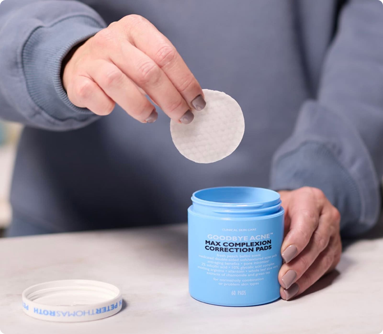 Person pulling a cotton pad from a blue container labeled 'Facial Cotton Pads'